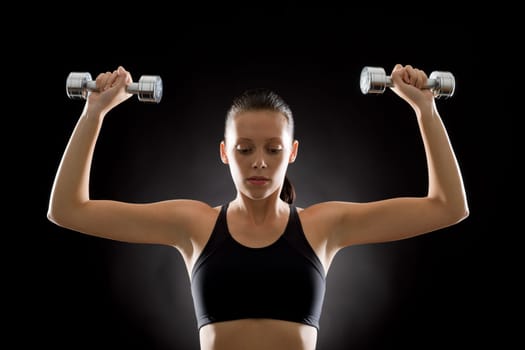 Portrait of sporty young woman holding dumbbells on black background