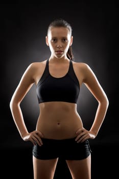 Portrait of sporty young woman standing akimbo on black background