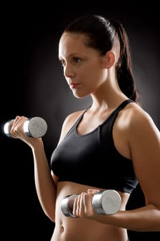 Sporty young woman holding dumbbells on black background
