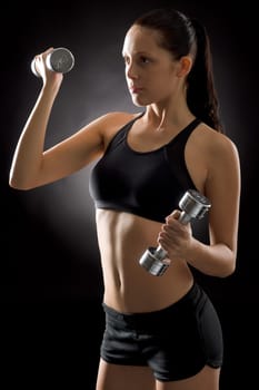 Sporty young woman holding dumbbells on black background