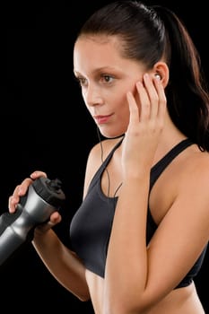 Sporty young woman with headphones and bottle on black background