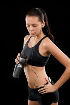 Sporty young woman with headphones and bottle on black background