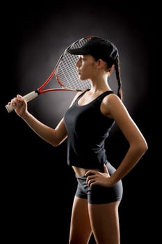 Young female tennis player posing with racket on black background