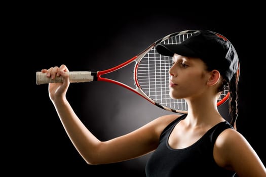 Young female tennis player posing with racket on black background