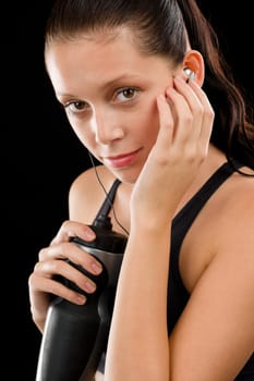 Young fitness woman with headphones and bottle on black background