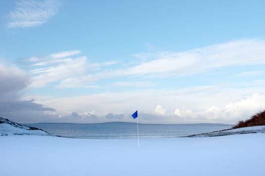 a snow covered links golf hole in ireland in winter evening weather with blue flag