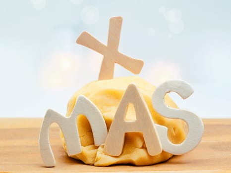 Baking Xmas cookies and biscuits with a mound of freshly prepared pastry left to rise on a wooden tabletop with the letters XMAS embedded in the dough