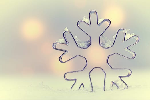 Ethereal snowflake Seasonal background with a snowflake-shaped metal cookie cutter oulined against soft muted Christmas lights with copysapce