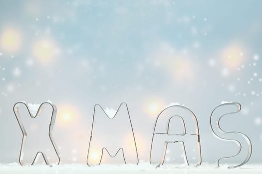 Metal Xmas cookie cutters standing in snow outlined against a soft blue atmospheric background with muted glowing lights and lots of copyspace for your Christmas greeting
