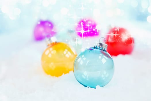 Delicate blue glass Christmas bauble on snow with additional twinkling colourful balls behind with shallow dof for a pretty wintery seasonal background