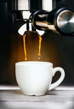 Closeup of a professional stainless steel coffee machine pouring freshly brewed aromatic espresso coffee into a plain white ceramic cup