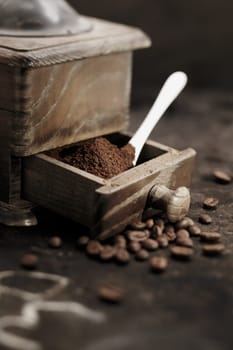Pile of fresh ground coffee grains in the open drawer of an old rustic wooden coffee grinder with a measuring spoon in a country kitchen