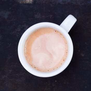 Overhead view of a hot frothy cup of cappuccino or cafe au lait standing on a slate blackboard in square format