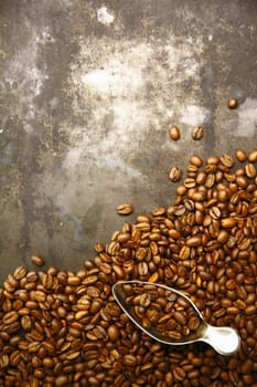 Scattered pile of aromatic fresh roasted coffee beans with a small metal scoop on a grunge background with copyspace