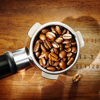 Coffee bean closeup detail and texture filling a metal filter from an espresso machine, overhead view on wood with stamped consignment numbers and vignetting