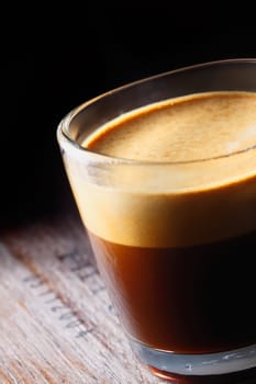 Cropped closeup of a frothy aromatic mug of fresh coffee in a glass mug on an old wooden table with shadowed background