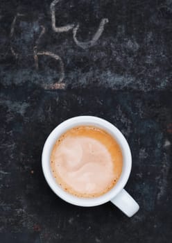 Overhead view of an aromatic frothy cup of freshly brewed cappuccino standing on a grungy old blackboard slate with chalk scribblings and copyspace