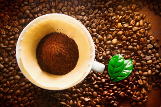 Overhead view of freshly ground coffee in a portable plastic filter on a bed of whole rich brown roasted coffee beans with copyspace