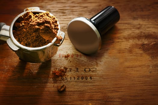 Freshly ground coffee beans in a metal filter on a wooden background with copyspace during preparation of a cup of aromatic filter coffee or espresso