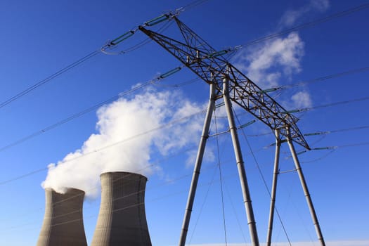 Chimneys of a nuclear power plant with a pylon for renewable energy on blue sky background