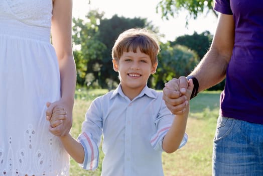 Family fun, happy mother, father and son holding hands in park and looking at camera. Waist up, front view