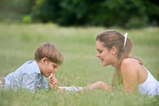 People and education, mother helping child with homework, lying on grass and reading book at park. Medium shot