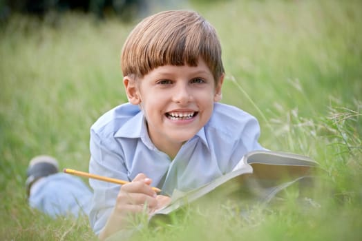 Young people and education, school child doing homework, laying down on grass at park and studying with book, smiling at camera