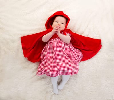 Baby Little Red Riding Hood on white fur lying with open cape