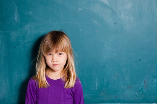 Portrait of a young girl standing in front of blank chalkboard