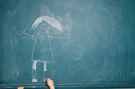 Child drawing image of smiling princess with crown on a chalkboard using piece of chalk