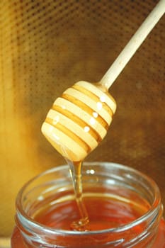 Honey dripping from a wooden honey dipper on honeycomb background