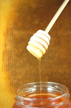Honey dripping from a wooden honey dipper on honeycomb background