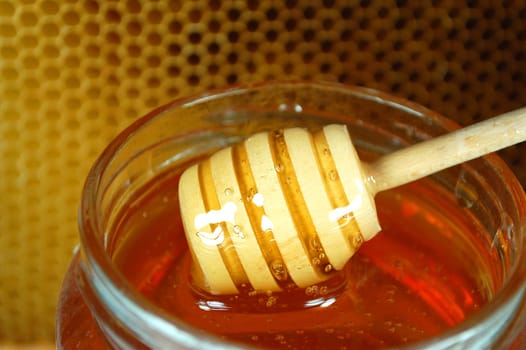 Honey dripping from a wooden honey dipper on honeycomb background