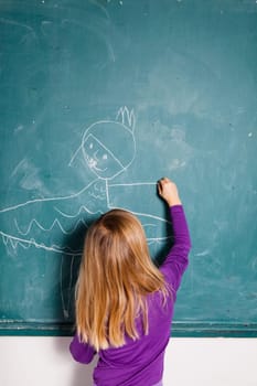 Studio portrait of young girl in classroom drawing image of girl in dress on a chalkboard