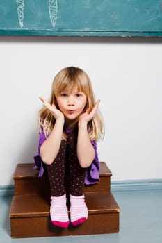 Studio portrait of young girl sitting in front of chalkboard in classroom blowing kiss