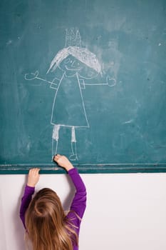 Studio portrait of young girl in classroom drawing image of princess with crown on a chalkboard