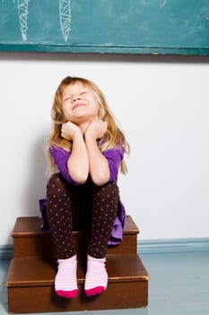 Studio portrait of smiling young girl sitting in front of chalkboard in classroom with eyes closed