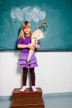 Studio portrait of young girl holding an umbrella while standing in front of chalkboard with image of rain cloud