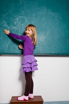 Studio portrait of smiling happy young girl in classroom drawing on a chalkboard