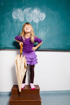 Studio portrait of smiling young girl holding an umbrella while standing in front of chalkboard with image of rain cloud