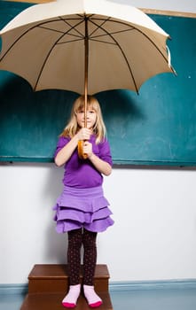 Studio portrait of young girl holding an umbrella while standing in front of chalkboard