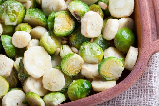 Roasted parsnips and brussel sprouts in terracota baking dish.