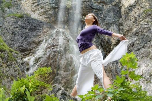 A young sporty woman exercising yoga exercises in front of a waterfall