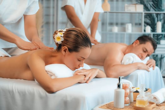 Caucasian couple customer enjoying relaxing anti-stress spa massage and pampering with beauty skin recreation leisure in day light ambient salon spa at luxury resort or hotel. Quiescent