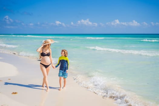 A radiant pregnant mother and her excited son share a tender moment on a serene, snow-white beach, celebrating family love amidst nature's beauty.