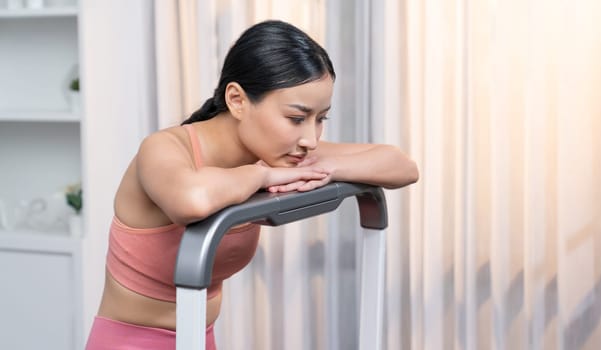 Energetic and strong athletic asian woman resting on elliptical running machine at home. Pursuit of fit physique and commitment to healthy lifestyle with home workout and training. Vigorous