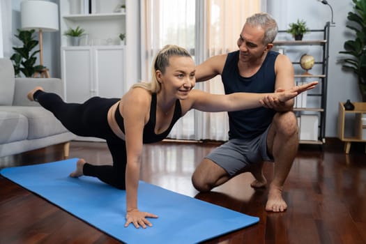 Happy active senior couple in sportswear being supportive and assist on yoga posture together at home. Healthy senior man and woman lifestyle with yoga exercise. Clout