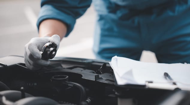 Male mechanic in garage, working on truck engine with dipstick. Horizontal photo of technician looking worried and distraught while checking liquid levels. Concept for car repair and insurance.