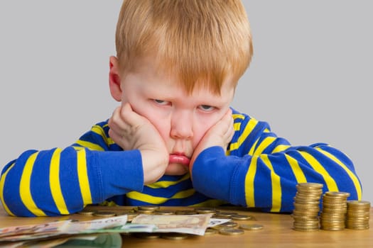 Child sits pouting in front of coins and bills