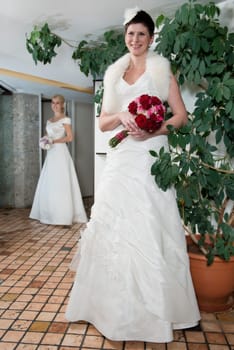 A bride with a headdress in a white dress and fur,behind her the bridesmaid